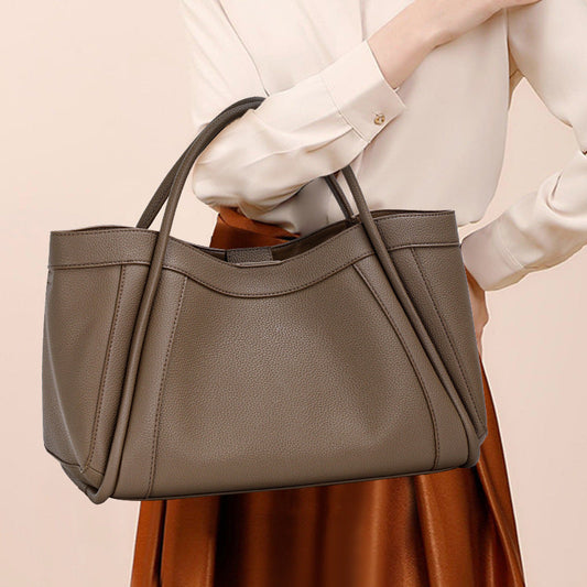 Person holding a brown handbag against a beige background