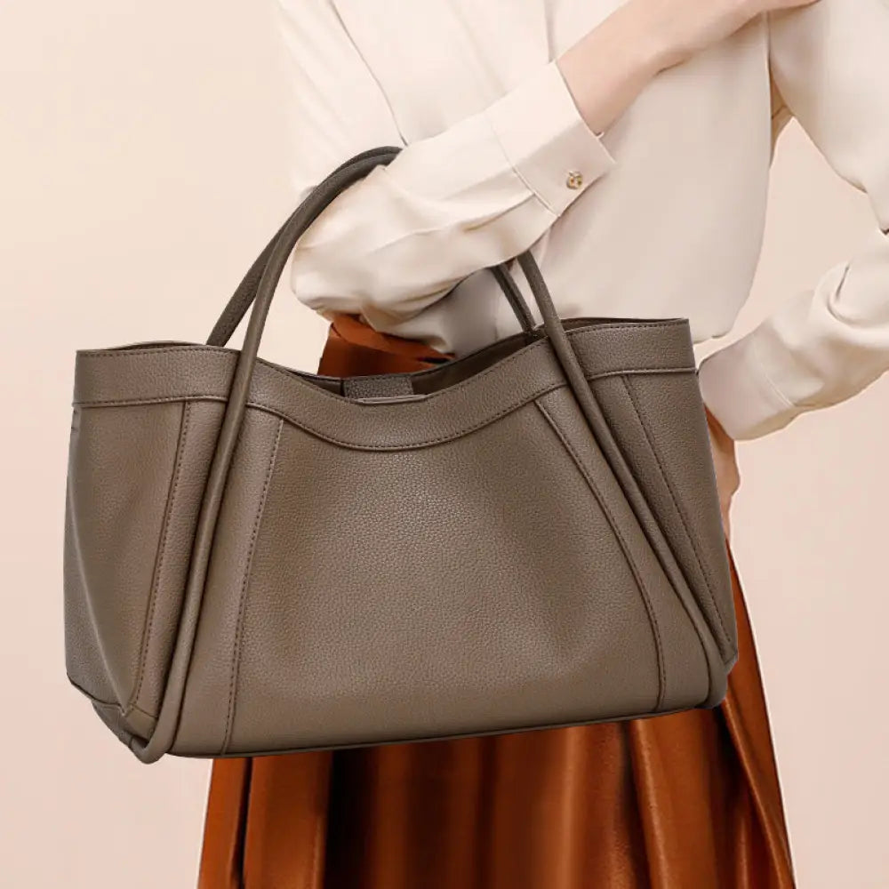 Person holding a brown handbag against a beige background