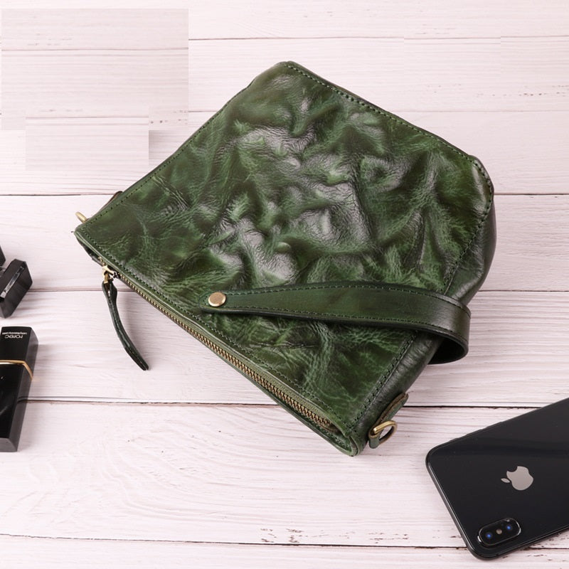 Green textured clutch bag on a white wooden surface with a phone and lipstick.