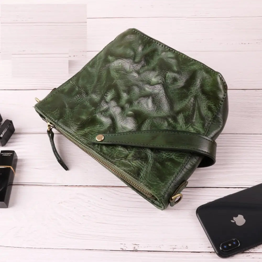 Green textured clutch bag on a white wooden surface with a phone and lipstick.