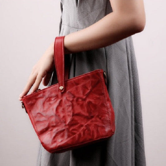 Red handbag held by a person wearing a gray dress on a light background